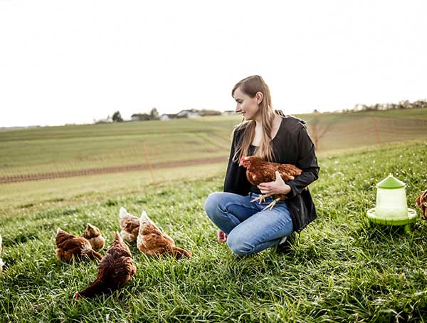 junge Frau hockend mit Huhn auf dem Arm